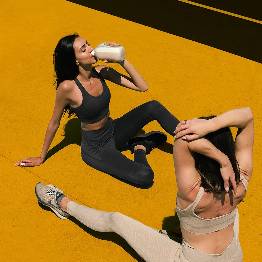 Stylised image of two female athletes drinking and posing in athletic wear on yellow background