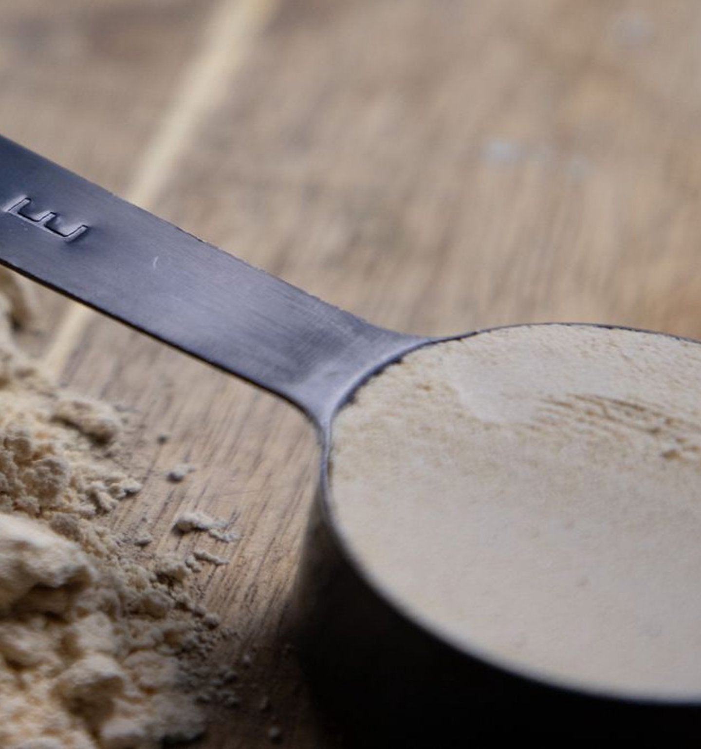 Protein powder scooped into RISE measuring spoon on wooden surface
